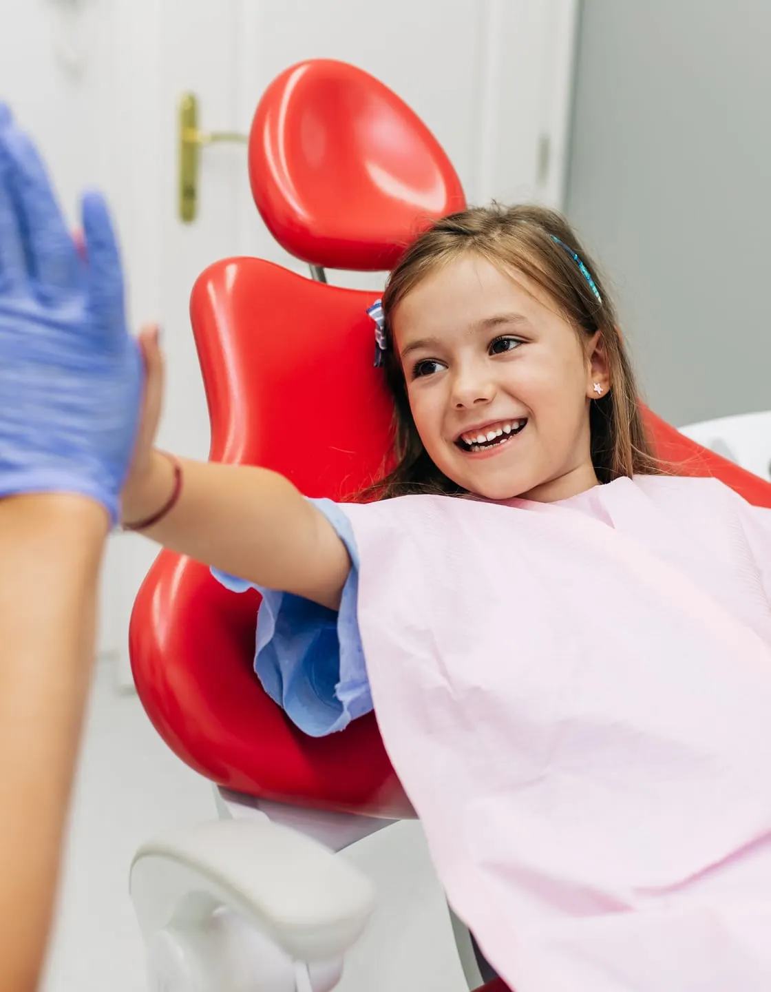 A girl in a dental chair giving a dentist a high five