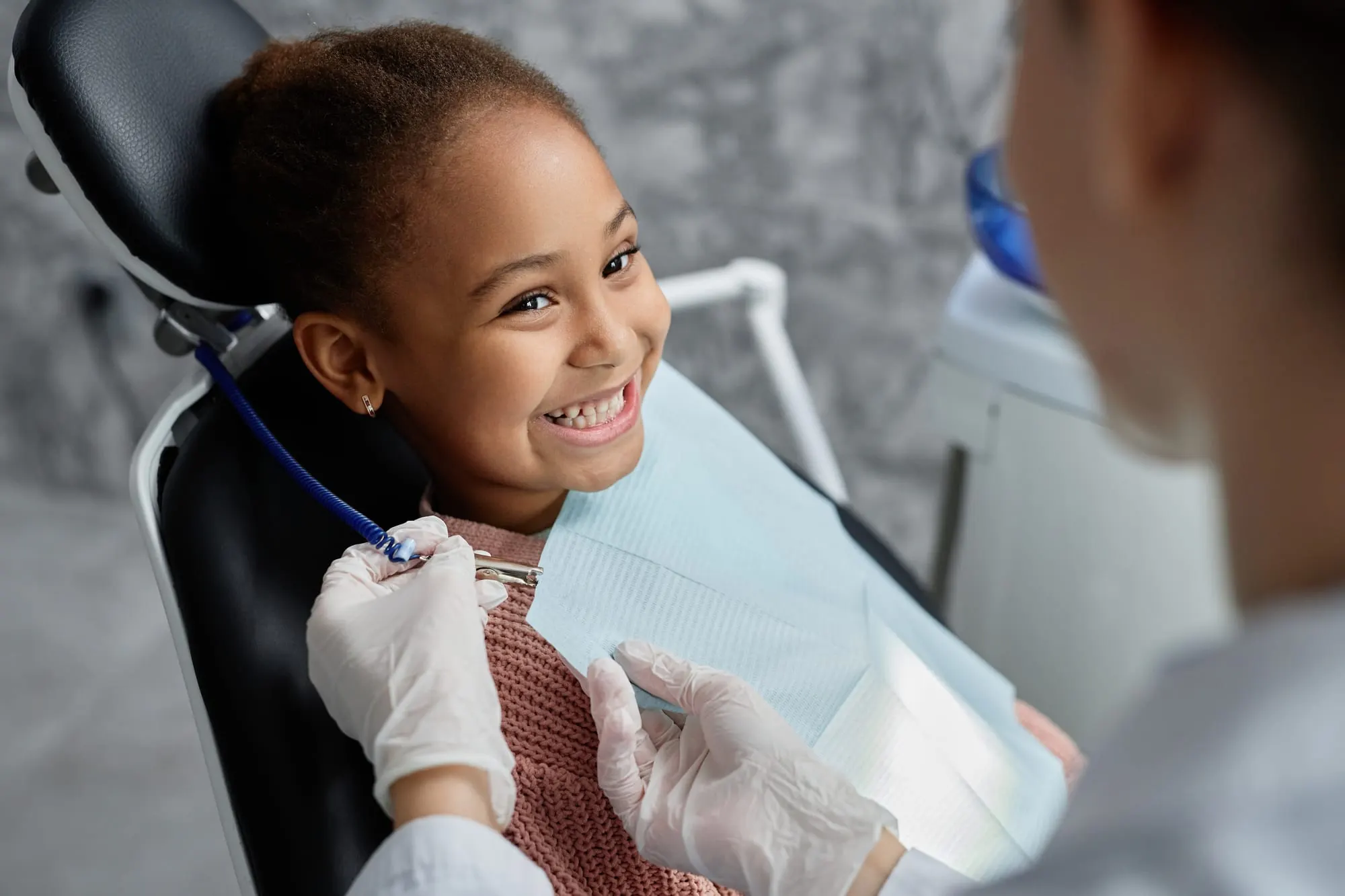 A smiling girl in a dental chair as a dentist begins treatment
